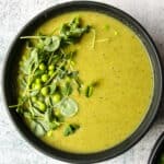 Bright green broccoli and pea soup in a black bowl.