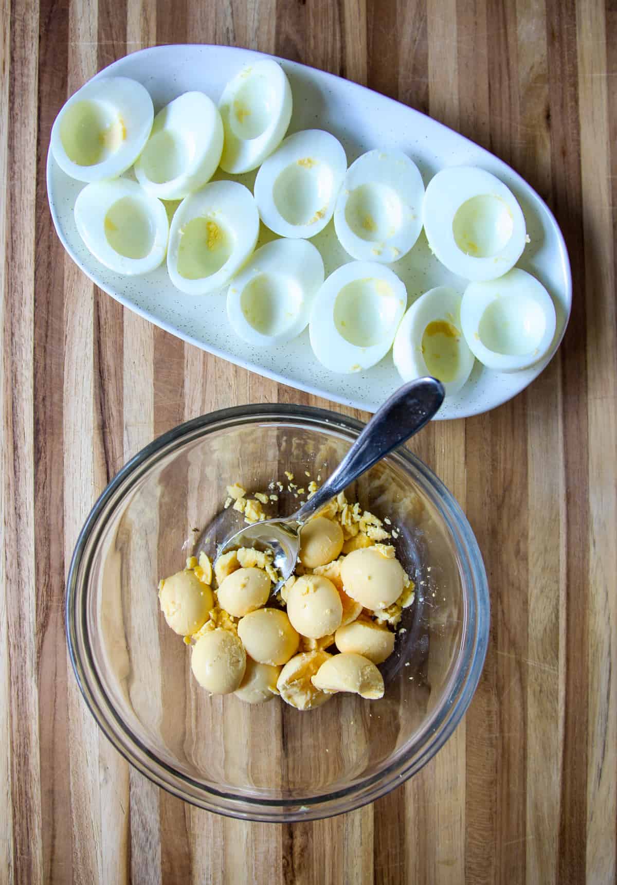 A dozen hard boiled egg halves with the yolks removed, next to a glass bowl containing the egg yolks.