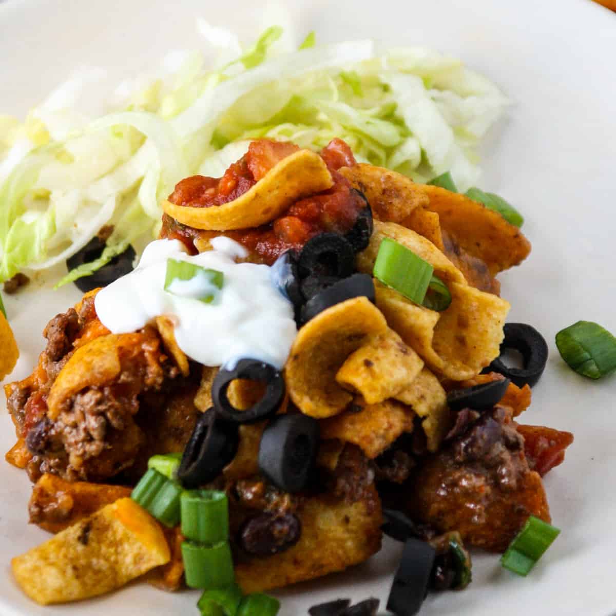 A slice of walking taco casserole on a white plate, garnished with green onion slices.