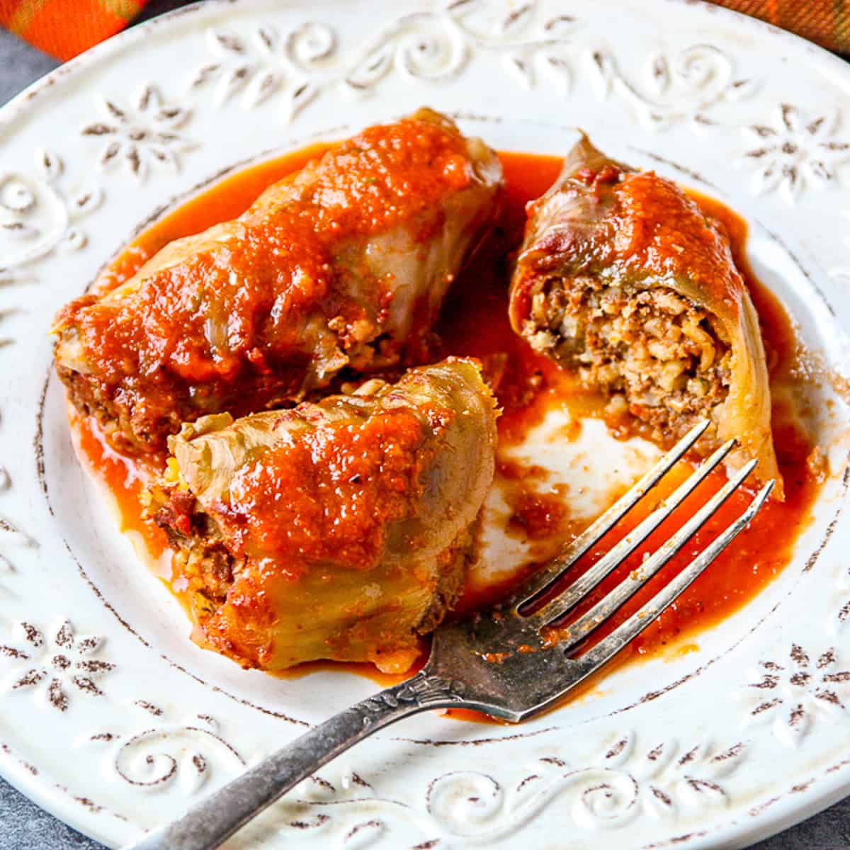 Two cabbage rolls on a white plate with a silver fork.