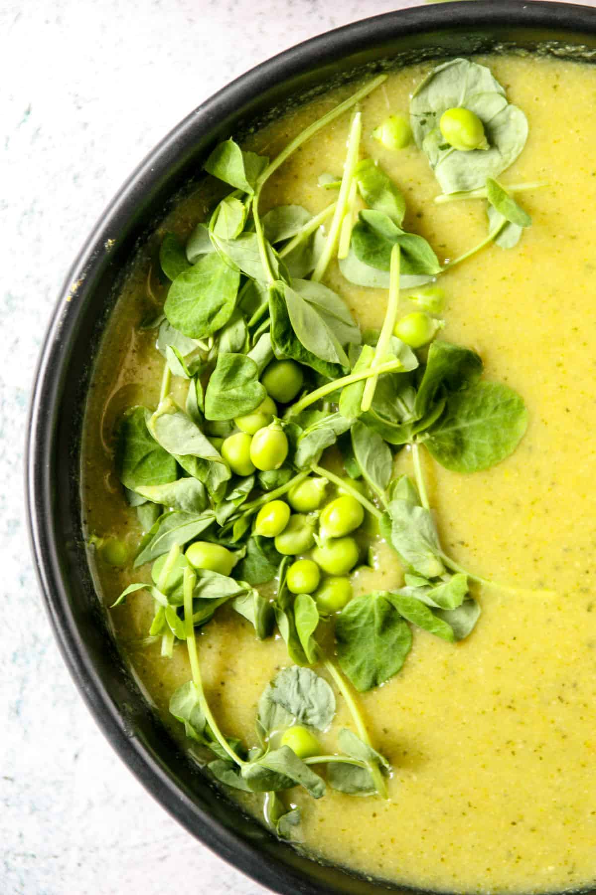 Bright green broccoli and pea soup in a black bowl.