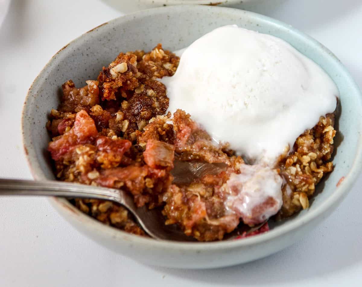Rhubarb crisp in a green dish, topped with a scoop of ice cream.