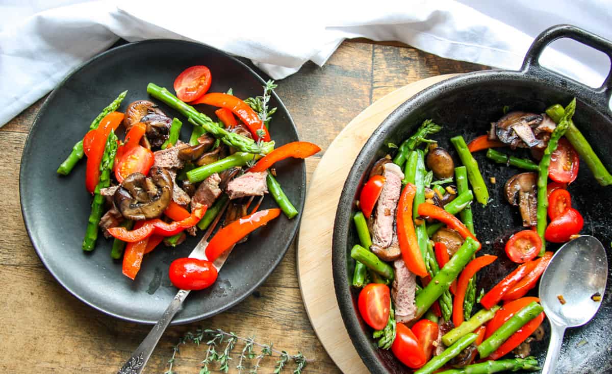 Steak and asparagus stir fry on a black plate.