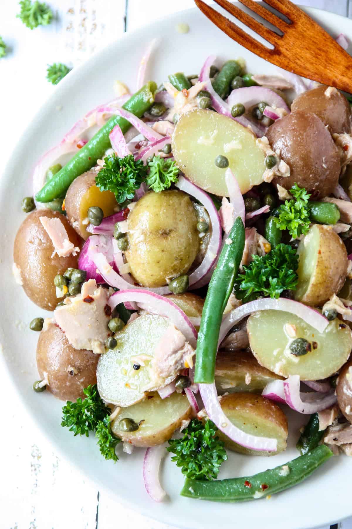 Tuna potato salad on a white plate with a wooden fork.
