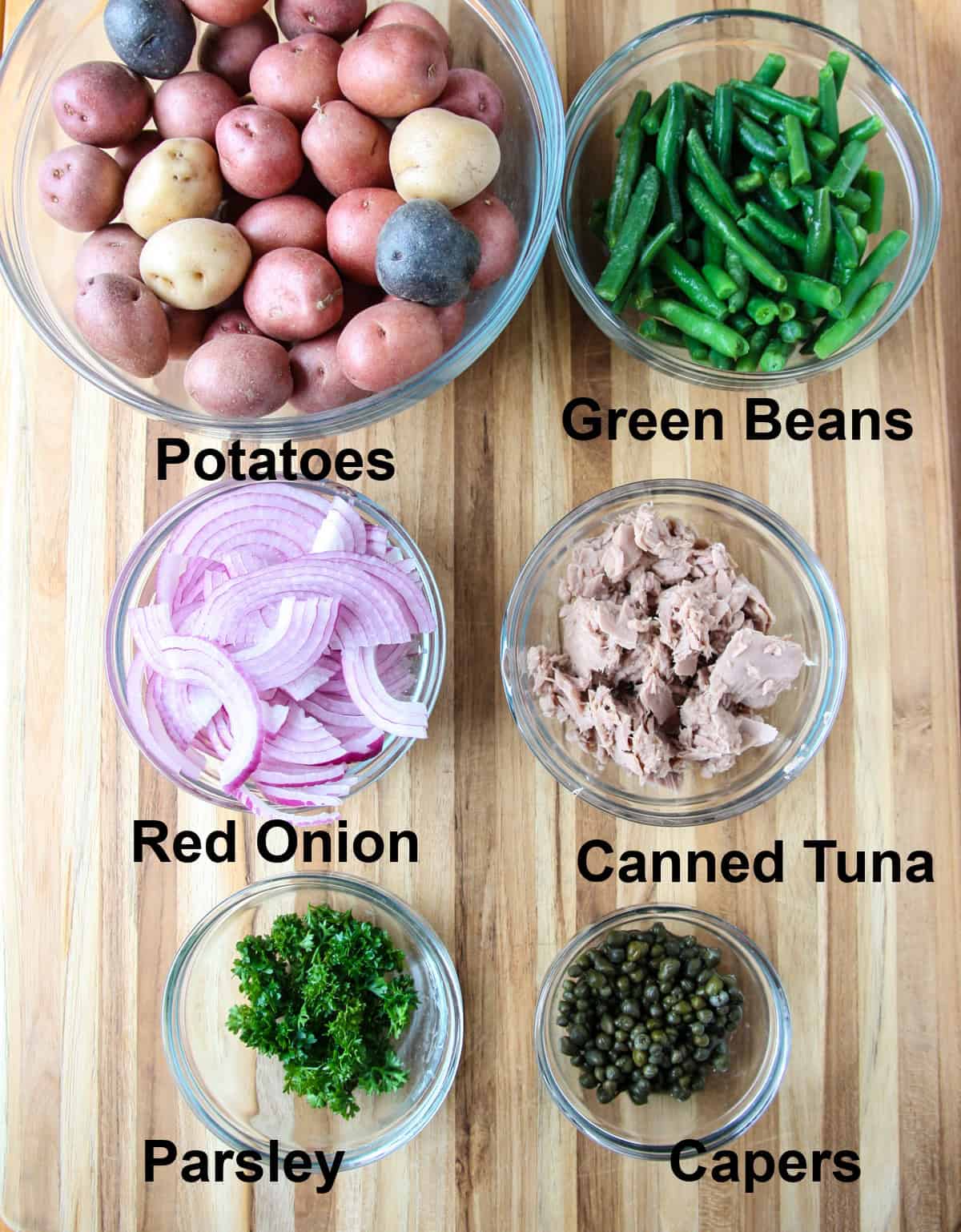The ingredients used to make this salad, in glass bowls on a wooden board.