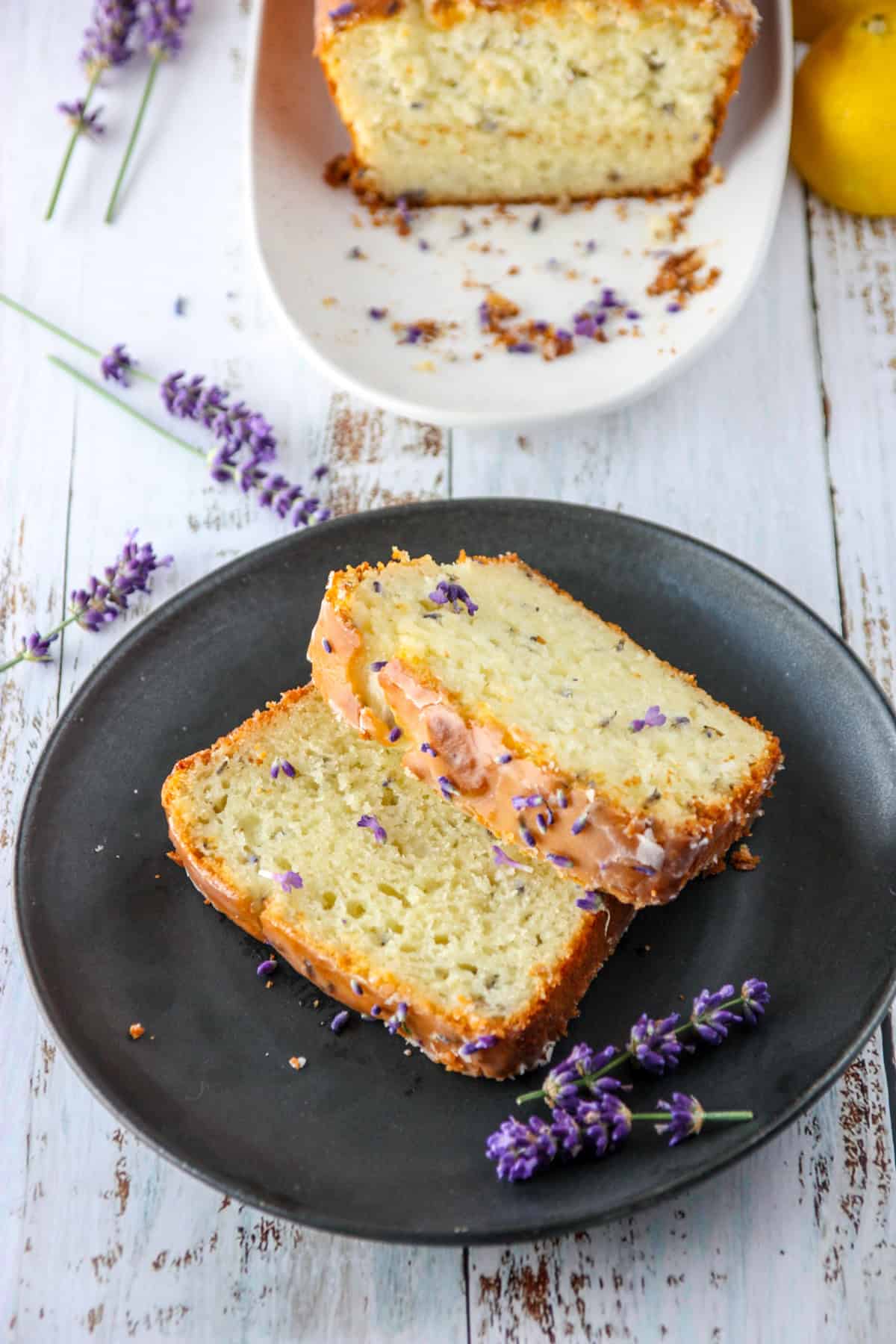 Two slices of lemon lavender cake on a black plate with a sprig of lavender.