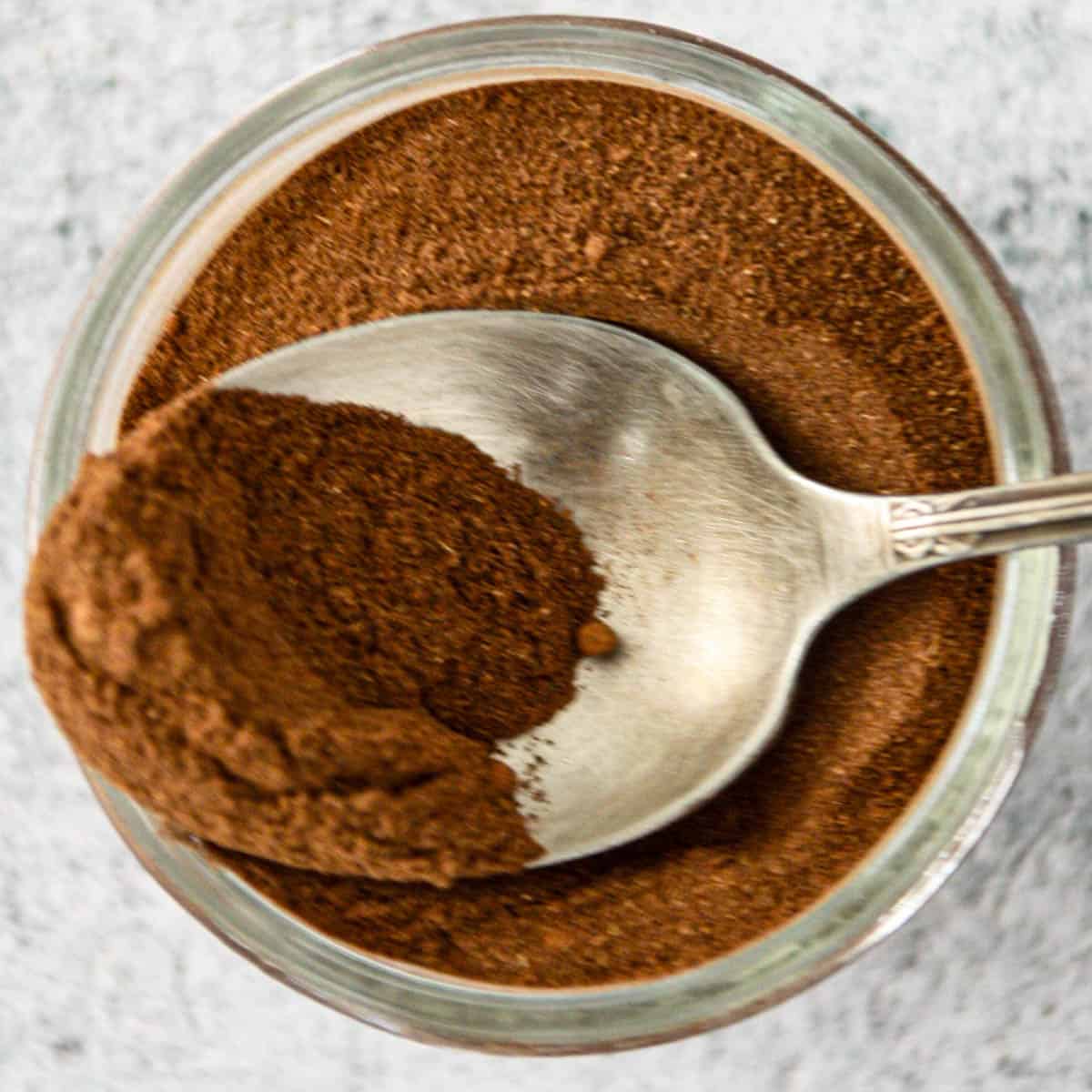 A jar of homemade pumpkin pie spice with a silver spoon.