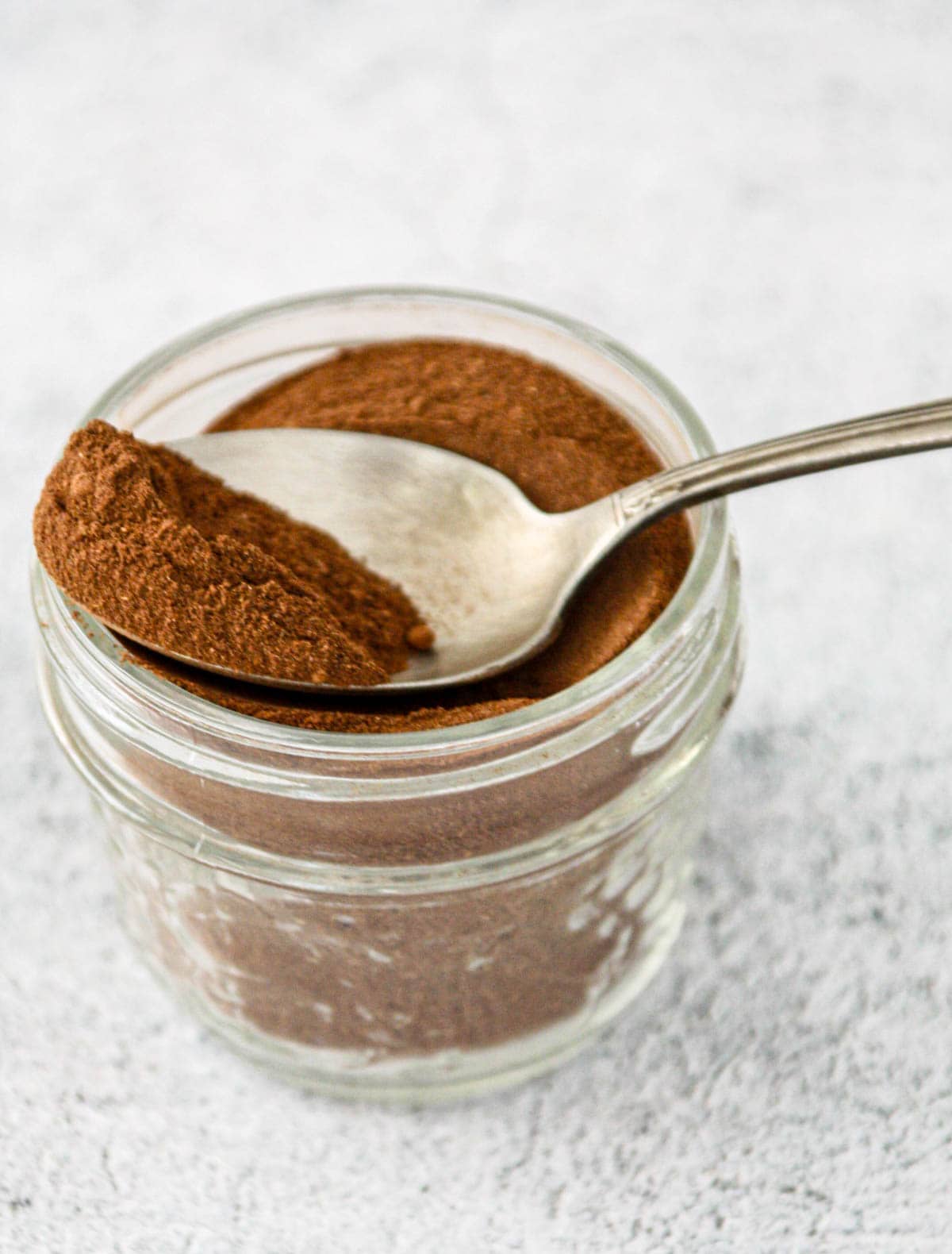 Homemade pumpkin pie spice in a glass jar with a spoon.
