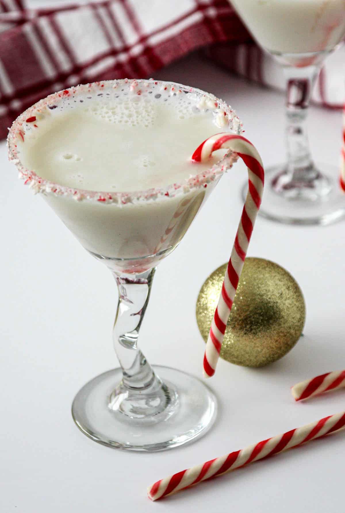 A candy cane martini in a glass garnished with crushed candy cane next to a gold Christmas ball.