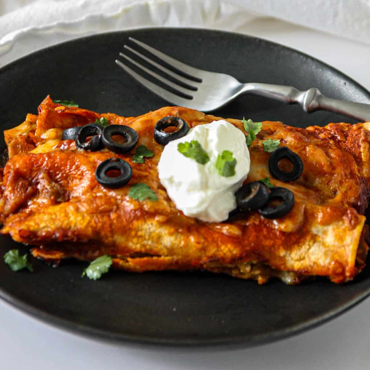 Two leftover turkey enchiladas on a black plate.