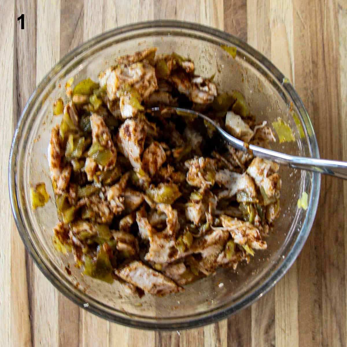 Turkey meat, green chiles and seasonings being mixed together in a glass bowl.