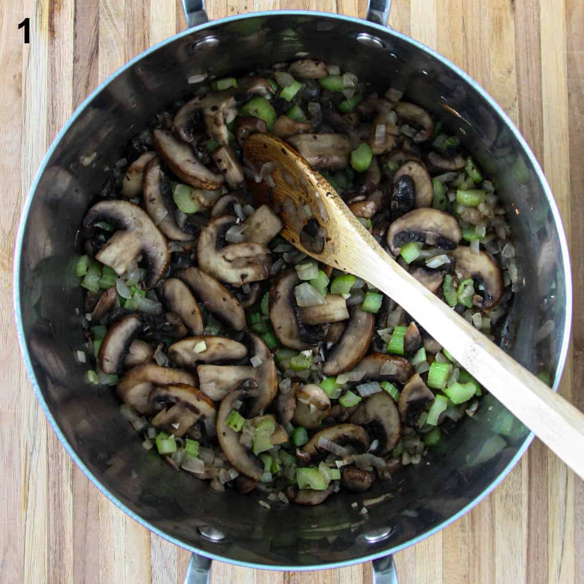 Mushroom slices, celery and onion in a soup pot with a wooden spoon.