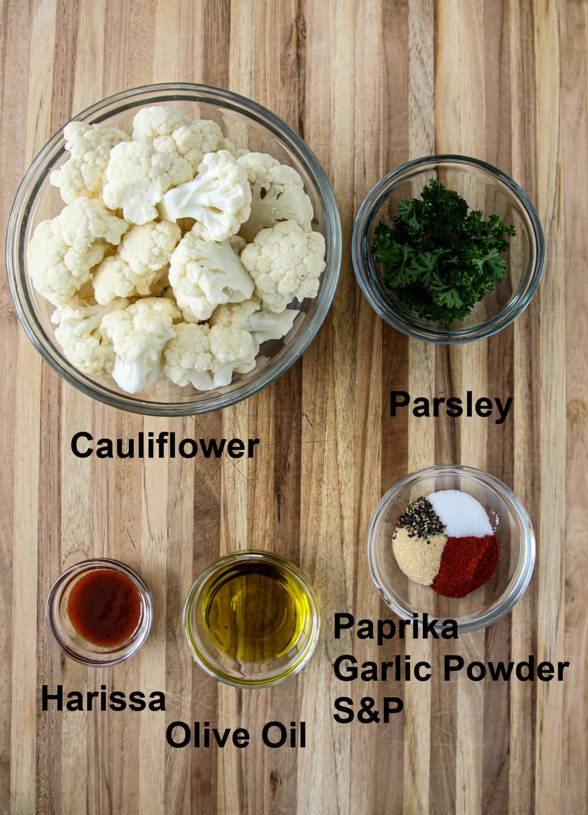 The ingredients for roasted cauliflower in glass dishes on a wooden board.