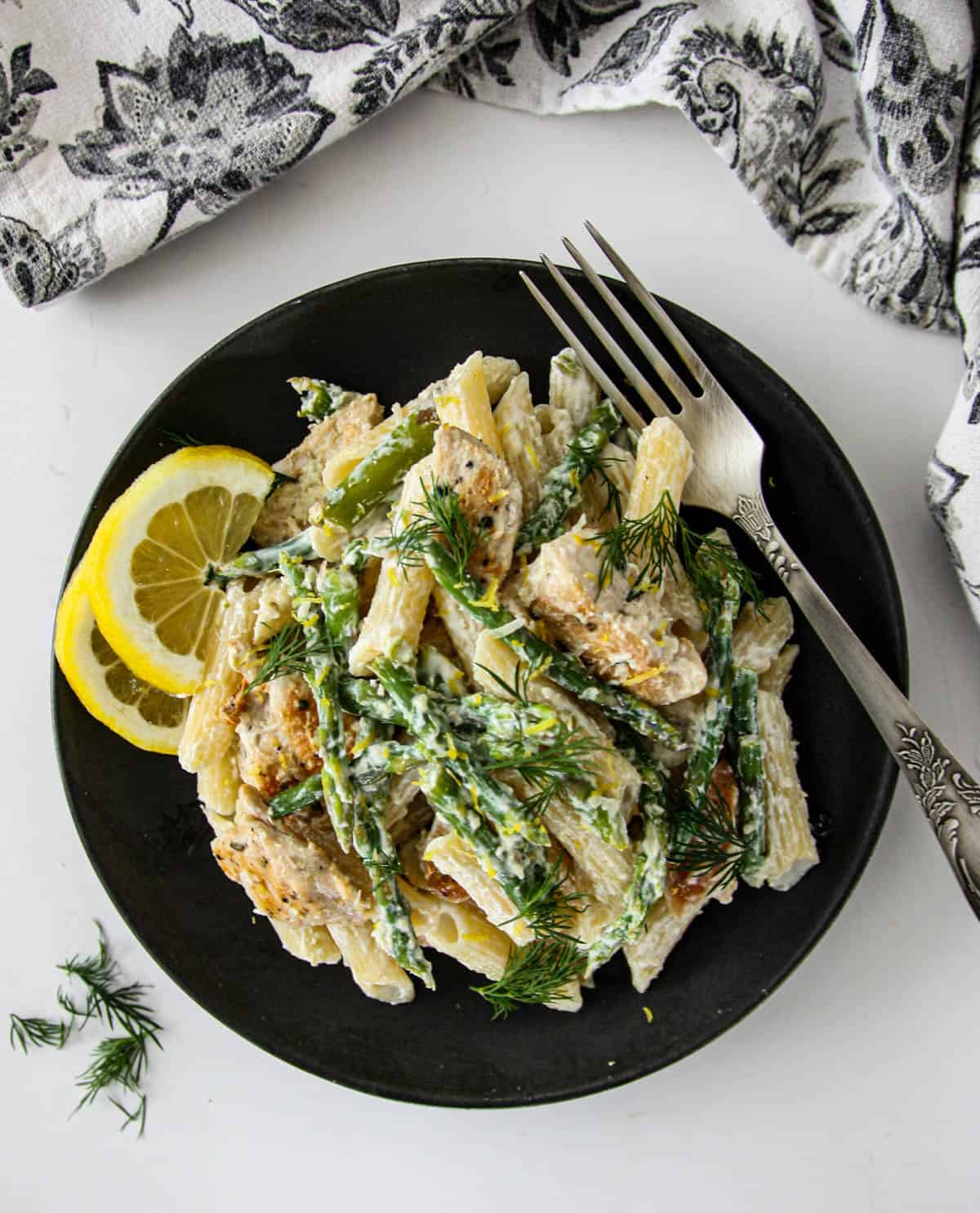 Asparagus and chicken pasta on a black plate with a silver fork.