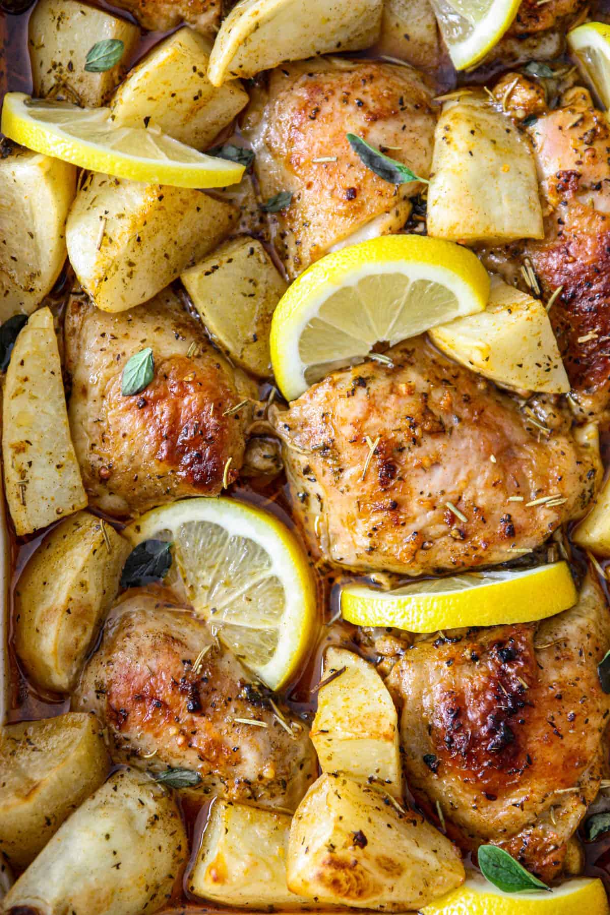 Greek lemon chicken and potatoes, garnished with lemon slices and oregano leaves.