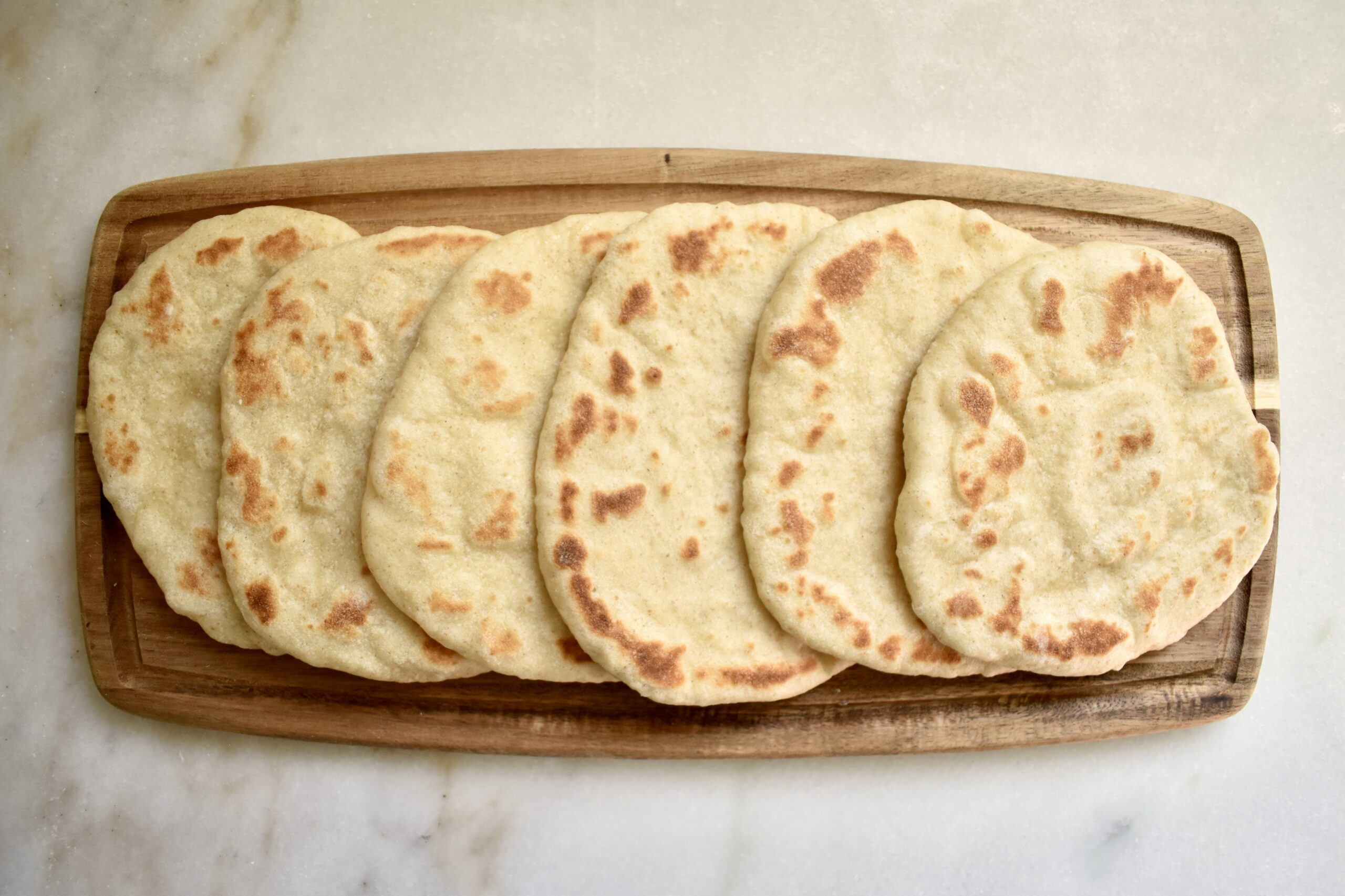 overhead view of naan bread pieces on a cutting board`