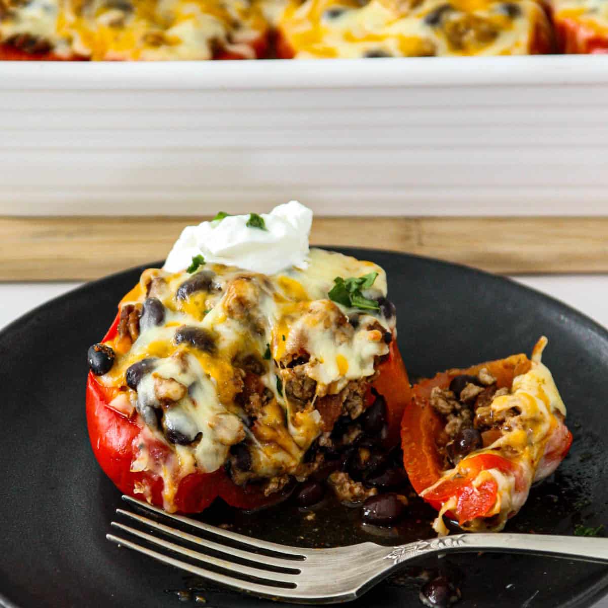 A taco stuffed pepper on a black plate with a silver spoon.