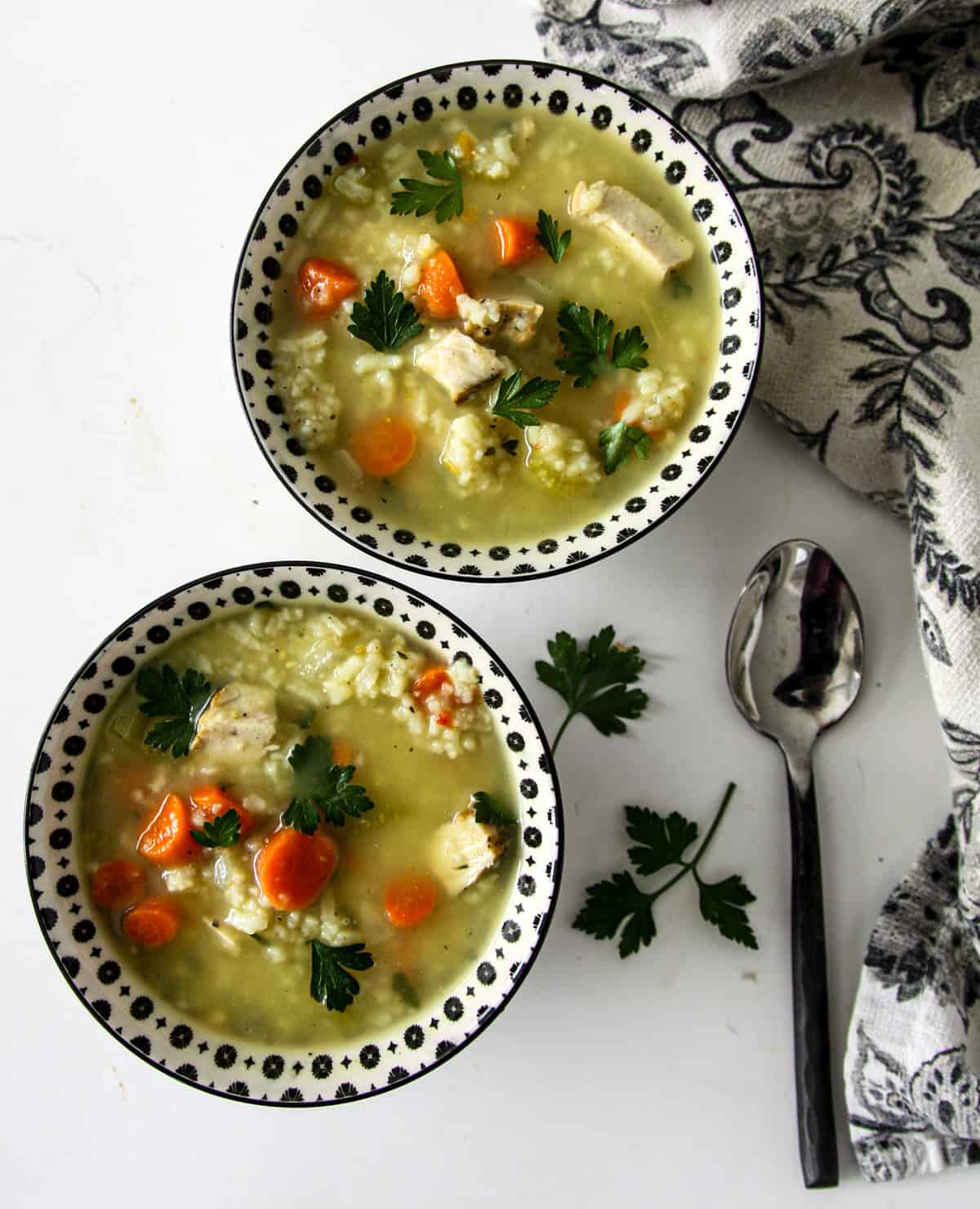 Two black and white bowls of turkey rice soup and a black metal spoon.