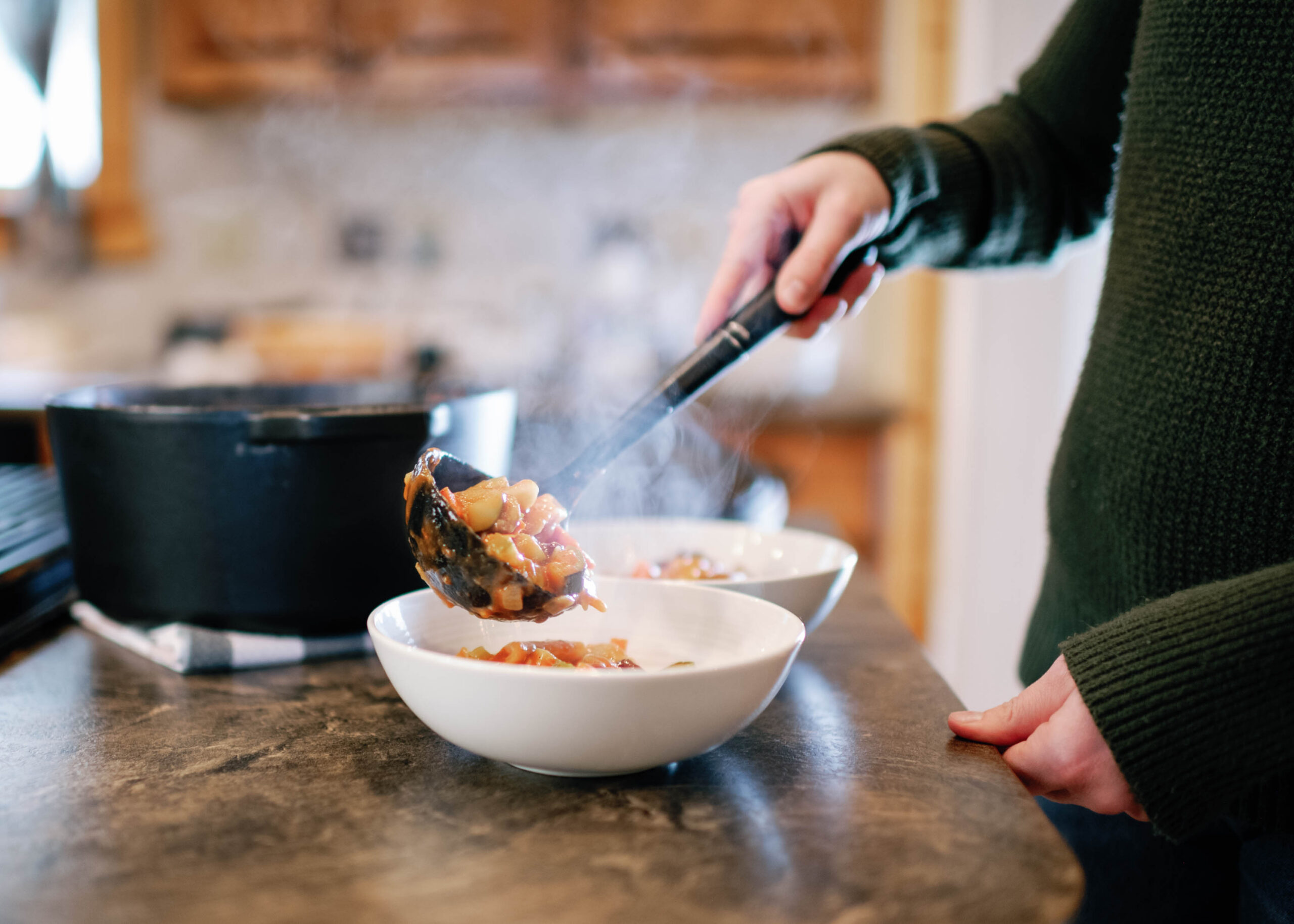 person laddeling stew into white bowls in a kitchen